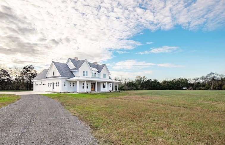 Three-quarter view of the white farmhouse beside a gravel drive