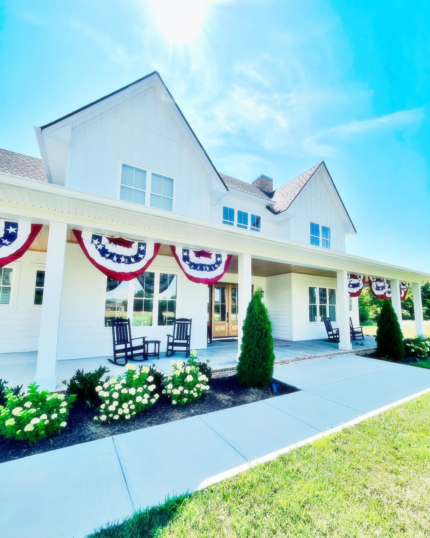 White farmhouse with a timber front door, porch chairs and flowering hydrangeas